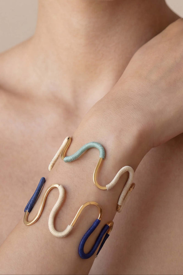 Woman wearing gold and blue hoop earrings and bracelets on a beige background