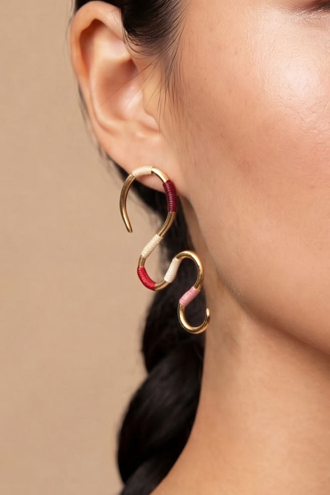 Woman with a neutral expression against a beige background wearing gold earrings

