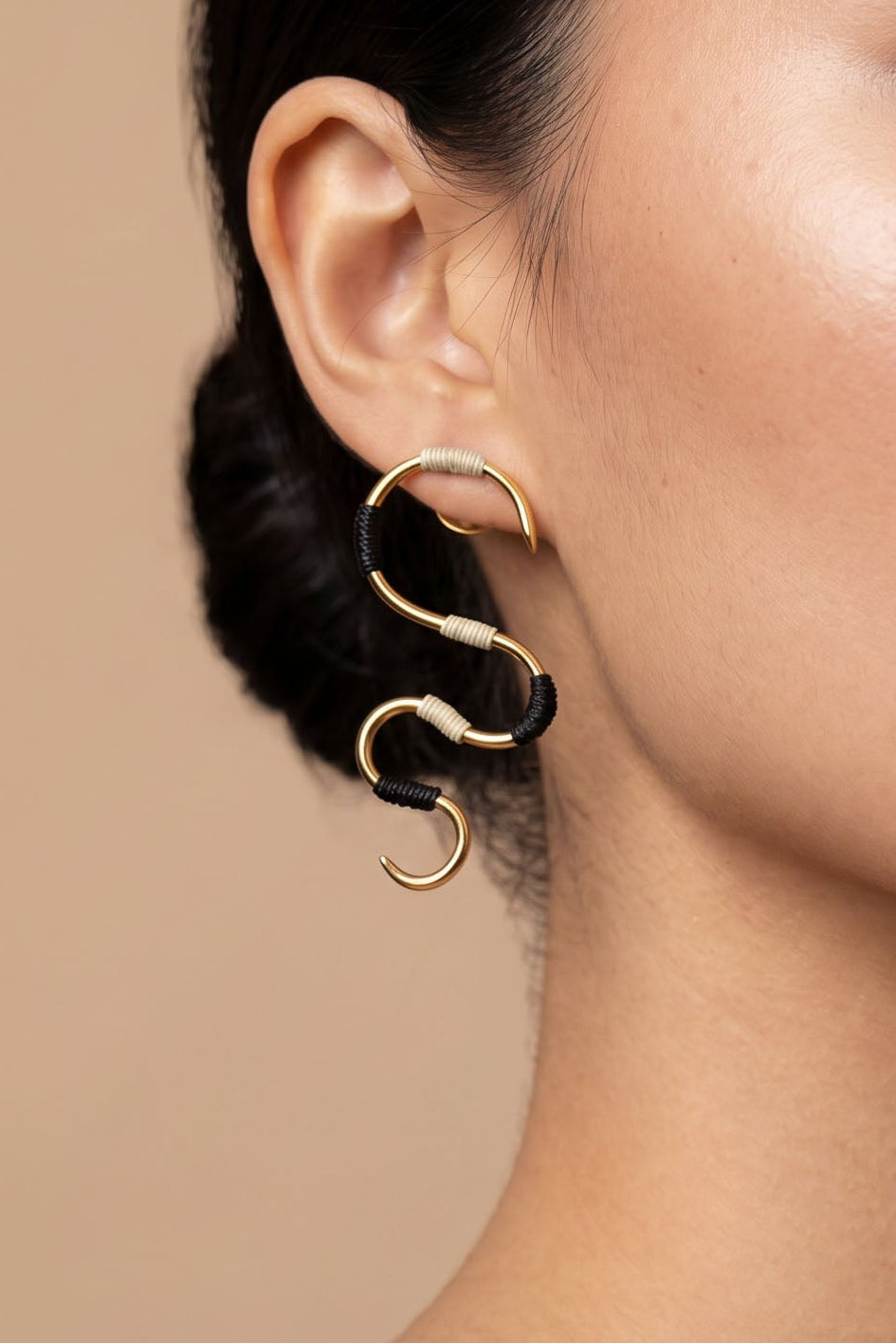 Gold hoop earrings with black hair ties worn by a person on a beige background