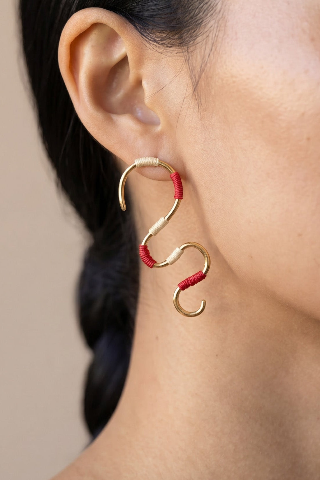 Close-up of a woman wearing a gold and red spiral earring against a neutral background